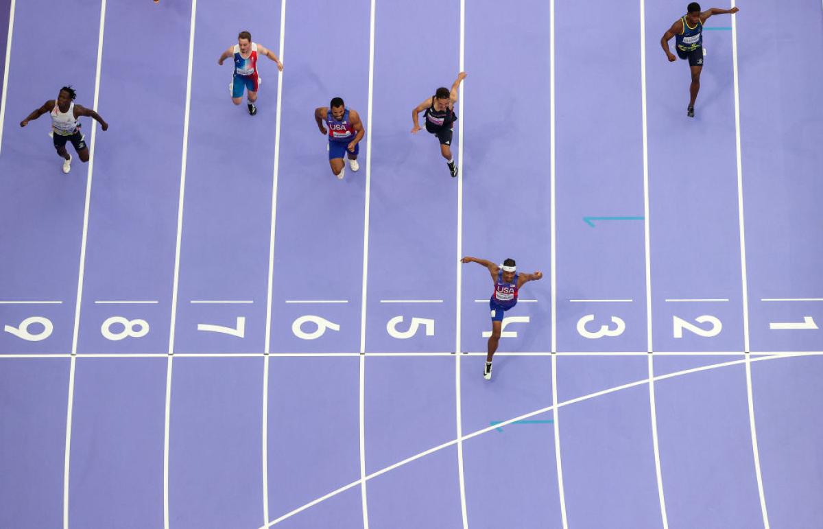 A photo taken from above shows purple athletics track and six athletes racing
